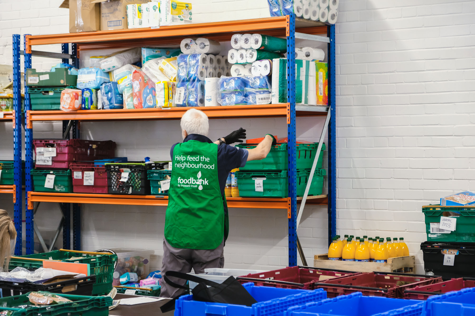 A volunteer grabs a crate off a shelf stacked with foodbank items at the warehouse