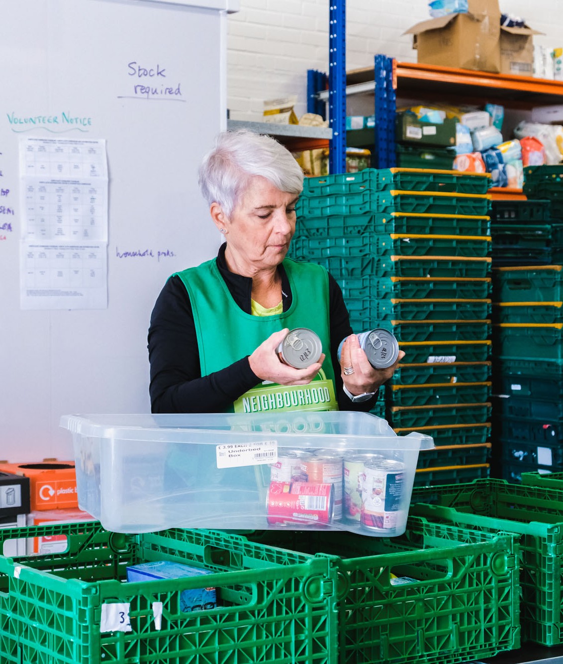 A volunteer looks at some tins of food while packing a crate