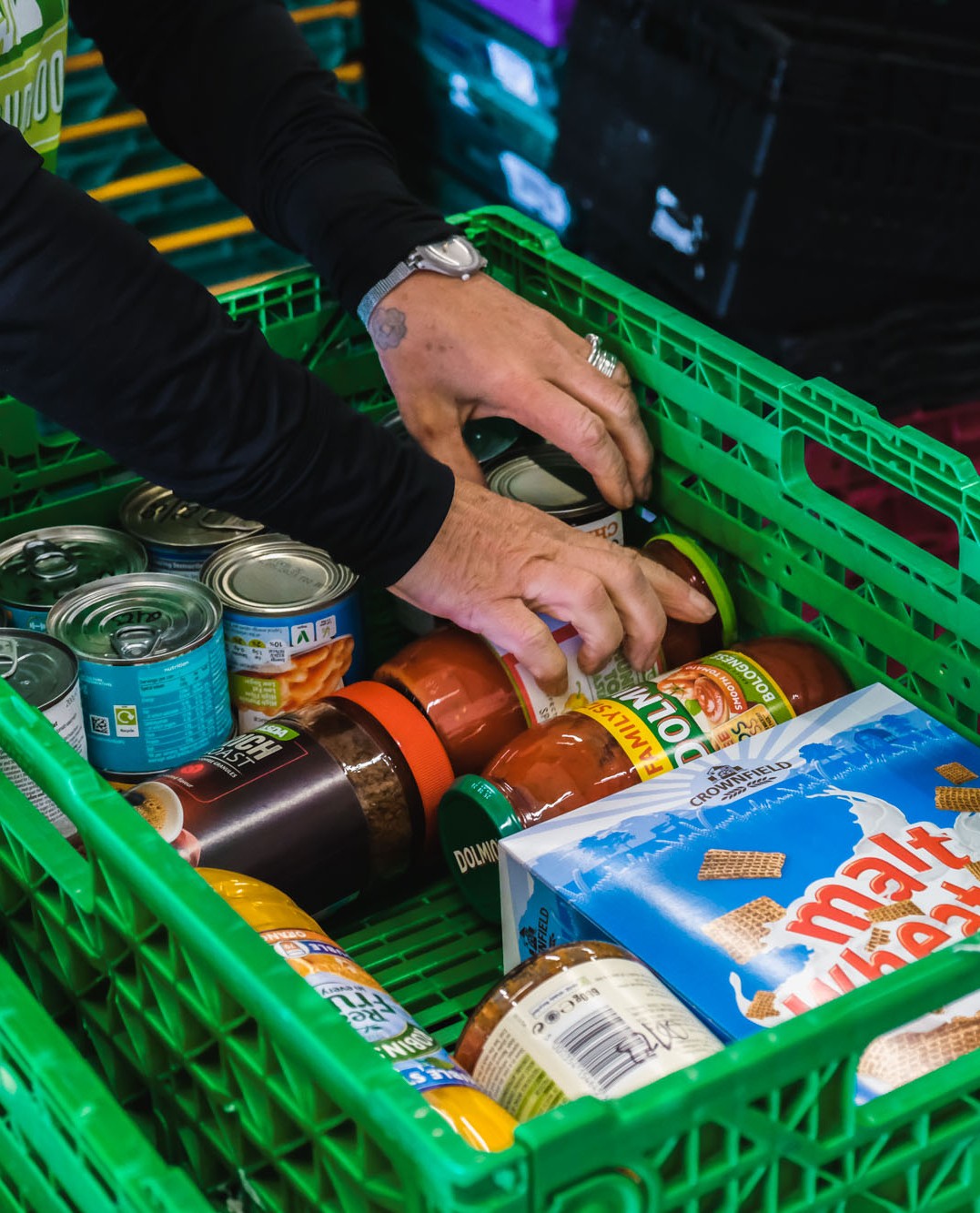 Hands pack a foodbank crate with jars, cereal and tins