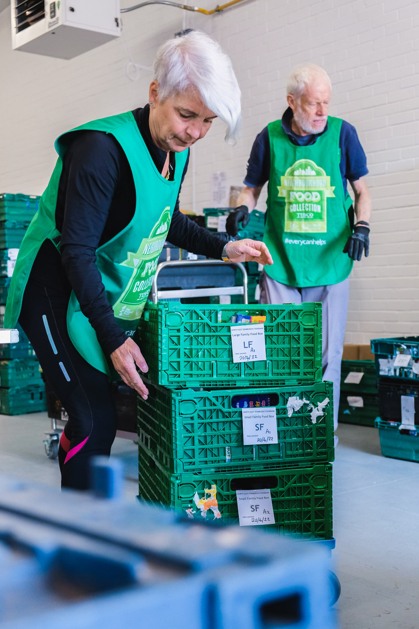Two volunteers work stack crates at the foodbank warehouse.
