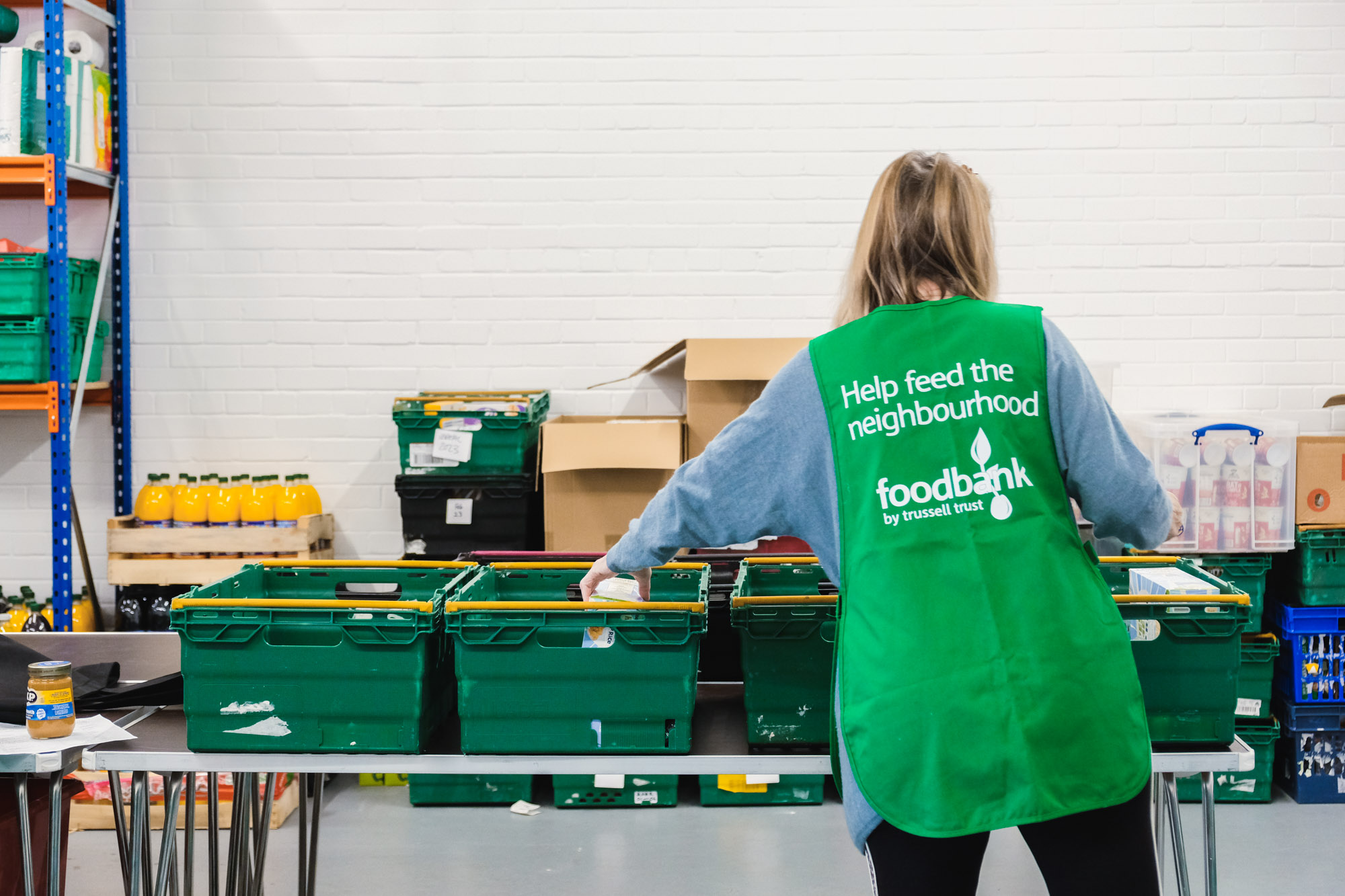 At the Edinburgh North East Foodbank, a volunteer distributes food into crates on a table.